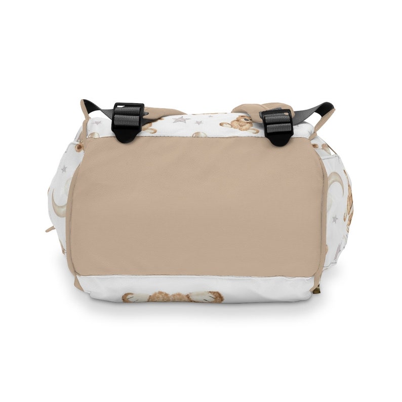 K&ouml;nnte beinhalten: Ein beige-wei&szlig;er Rucksack mit einem Muster aus B&auml;ren, Monden und Sternen. Der Rucksack hat verstellbare Tr&auml;ger und einen Rei&szlig;verschluss.