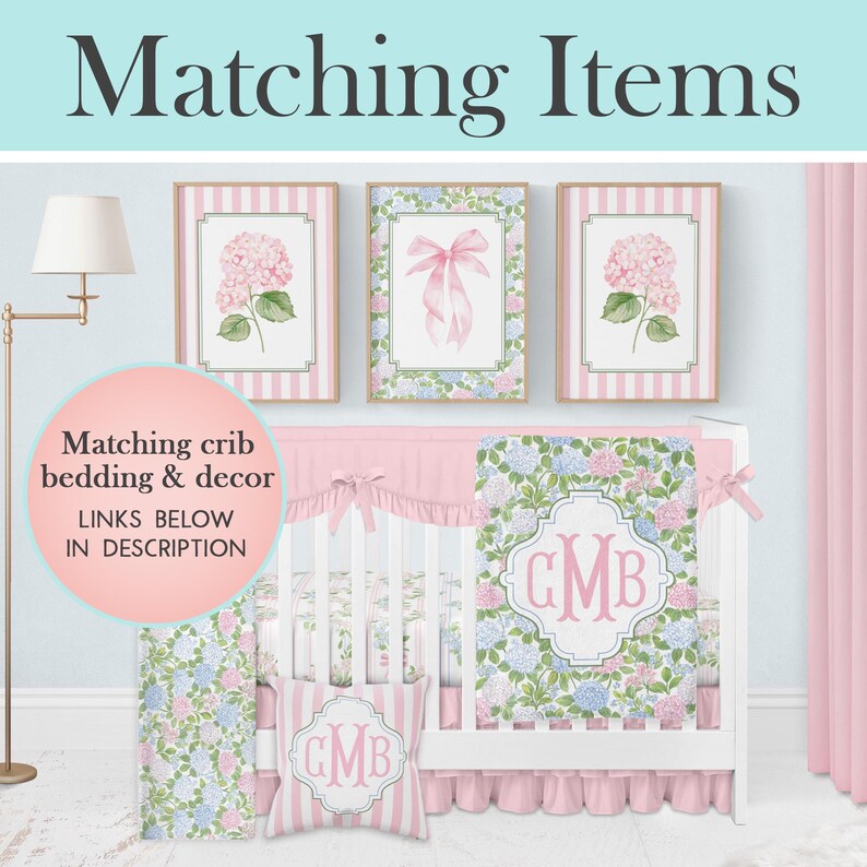 Puede incluir: Una cuna blanca con una manta de estampado floral con un monograma rosa, una almohada a rayas a juego con un monograma y tres cuadros de pared con hortensias rosas y un lazo rosa, con el texto Matching Items.