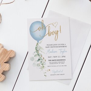 May include: A baby shower invitation with a blue balloon and gold lettering that says "Oh boy!" The invitation is decorated with watercolor greenery and gold glitter. The text on the invitation includes the name "Madison Taylor", the date "Sat | Nov 12 | 2PM", the location "The Smith Residence", and the address "1502 Wando Park Blvd, Charleston, SC 29407". The invitation also includes the RSVP information and the registry information.