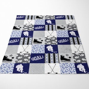 May include: A blue and gray patchwork quilt with a hockey theme. The quilt features hockey sticks, skates, and the word "GOAL!" repeated throughout.