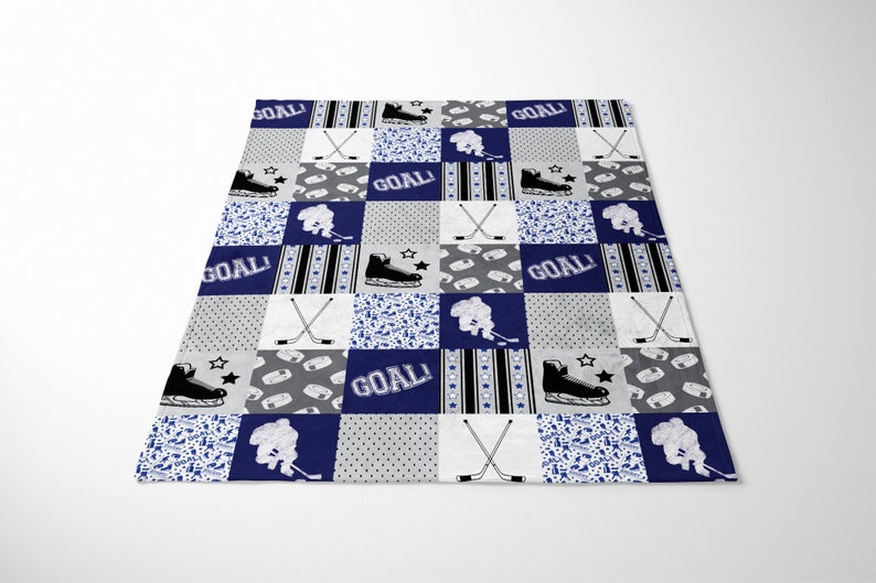 May include: A blue and gray patchwork quilt with a hockey theme. The quilt features hockey sticks, skates, and the word "GOAL!" repeated throughout.