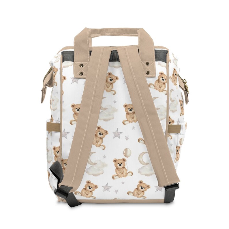 K&ouml;nnte beinhalten: Ein beigefarbener Canvas-Rucksack mit verstellbaren Tr&auml;gern. Der Rucksack hat ein wei&szlig;es Stofffutter mit einem sich wiederholenden Muster aus braunen Teddyb&auml;ren, Wolken und Sternen.