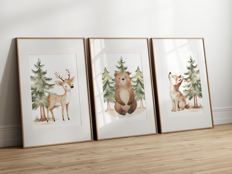 Op de afbeelding: Drie ingelijste aquarelprints met bosdieren. De eerste print toont een hert met geweien, de tweede een beer en de derde een vos. Elke print bevat groenblijvende bomen en een lichtbruine achtergrond.
