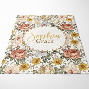 Op de afbeelding: Een wit bloemenkleed met een gouden cirkel in het midden. De cirkel heeft de naam "Sophia Grace" in gouden letters.