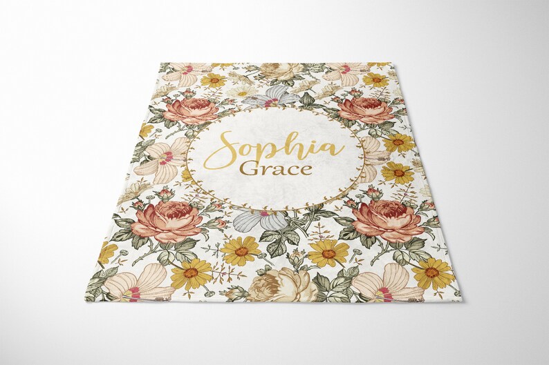 Op de afbeelding: Een wit bloemenkleed met een gouden cirkel in het midden. De cirkel heeft de naam "Sophia Grace" in gouden letters.