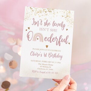 May include: A pink and gold birthday invitation with a rainbow and the text "Isn't she lovely, Isn't she O-nederful." The invitation is for Claire's 1st birthday party.