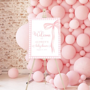 May include: Pink and white gingham welcome sign with a pink watercolor bow and the text "Welcome to Audrey's Baby Shower August 17, 2024".