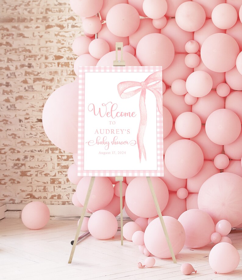 May include: Pink and white gingham welcome sign with a pink watercolor bow and the text "Welcome to Audrey's Baby Shower August 17, 2024".