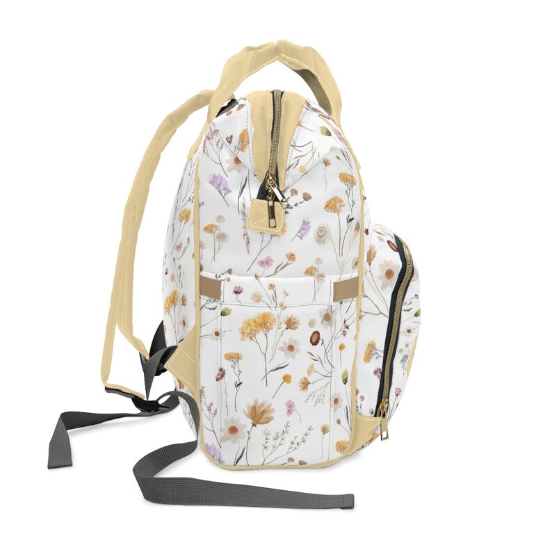 May include: A white and cream floral print diaper bag backpack with a cream zipper and a small zippered pocket on the side. The bag has adjustable straps and a top handle.