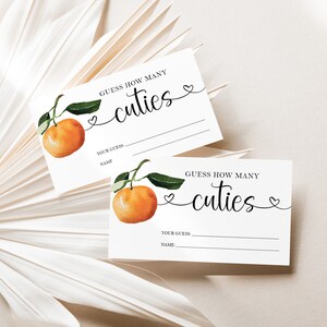 May include: Two white cards with a watercolor illustration of a mandarin orange. The text on the cards reads "Guess how many cuties".