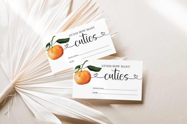 May include: Two white cards with a watercolor illustration of a mandarin orange. The text on the cards reads "Guess how many cuties".