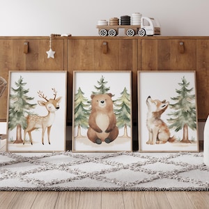 Op de afbeelding: Drie ingelijste aquarelprints met bosdieren: een hert, een beer en een wolf. Elke print heeft een lichte achtergrond met groene bomen. De prints worden tentoongesteld op een houten kast boven een grijs tapijt.