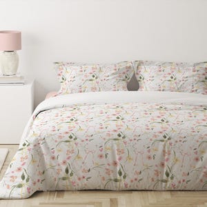 May include: A white duvet cover with a floral pattern featuring pink and yellow flowers and green leaves. The duvet cover is on a bed with two matching pillowcases.