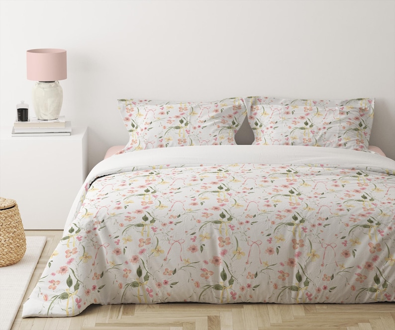 May include: A white duvet cover with a floral pattern featuring pink and yellow flowers and green leaves. The duvet cover is on a bed with two matching pillowcases.
