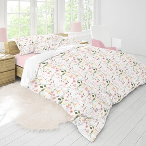 May include: A white duvet cover with a floral pattern featuring pink and yellow flowers on a white background. The duvet cover is on a bed with pink and white pillows.