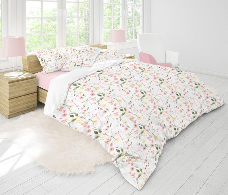 May include: A white duvet cover with a floral pattern featuring pink and yellow flowers on a white background. The duvet cover is on a bed with pink and white pillows.