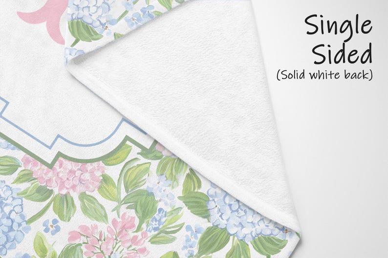 Puede incluir: Una manta de una sola cara con reverso blanco s&oacute;lido y un patr&oacute;n floral en el frente que presenta racimos de hortensias rosas y azul claro con hojas verdes. El texto "Single Sided (Solid white back)" est&aacute; impreso en negro a la derecha.