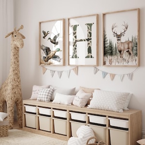 May include: A children's room scene featuring framed art prints with a woodland theme. The prints depict ducks, a camouflage letter "H", and a deer. A woven giraffe and storage bench with bins complete the decor.
