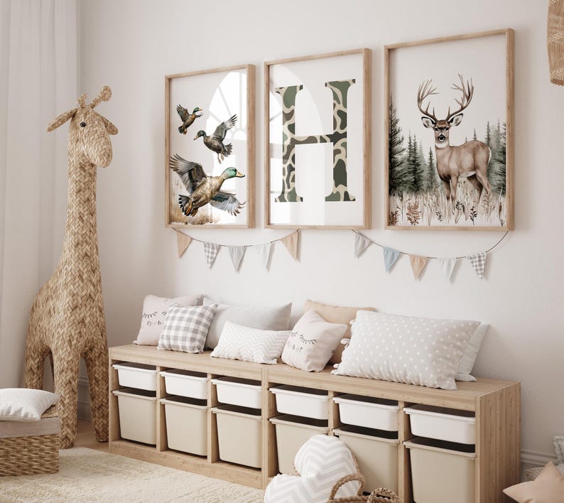 May include: A children's room scene featuring framed art prints with a woodland theme. The prints depict ducks, a camouflage letter "H", and a deer. A woven giraffe and storage bench with bins complete the decor.