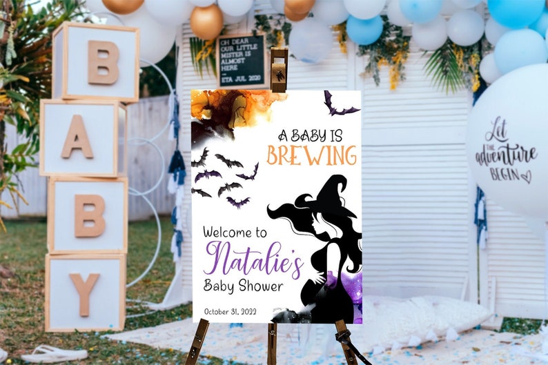Op de afbeelding: Een wit bord met een zwart silhouet van een zwangere heks op een paarse en oranje aquarel achtergrond. Het bord zegt "A Baby is Brewing" en "Welcome to Natalie's Baby Shower" met de datum "October 31, 2022".