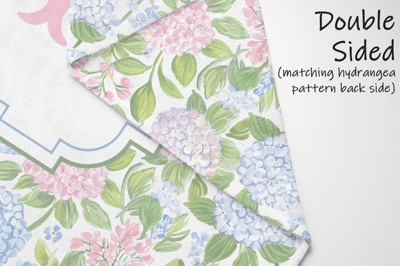 Puede incluir: Un tejido con un estampado floral de flores de hortensia rosas y azules con hojas verdes sobre un fondo blanco. La tela est&aacute; doblada para mostrar un patr&oacute;n de hortensias a juego en el reverso. El texto en la imagen dice Double Sided.