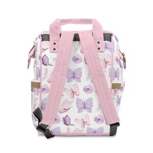 May include: Pink backpack with adjustable straps and a white background featuring a watercolour butterfly pattern. The backpack has two side pockets and a top handle.