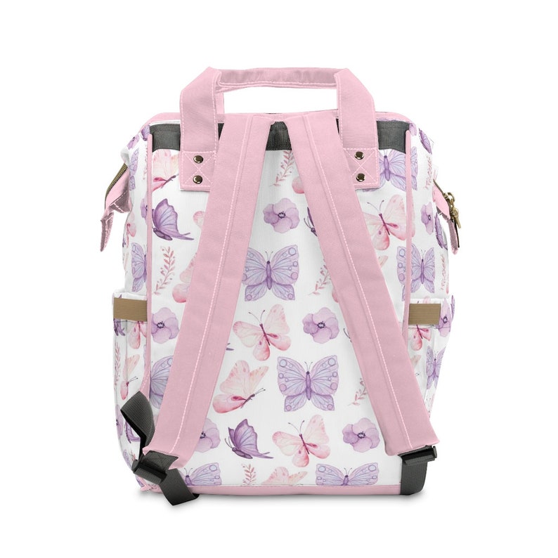 May include: Pink backpack with adjustable straps and a white background featuring a watercolour butterfly pattern. The backpack has two side pockets and a top handle.