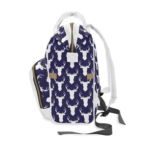 May include: A white backpack with a navy blue deer print. The backpack has a zipper closure and adjustable straps.