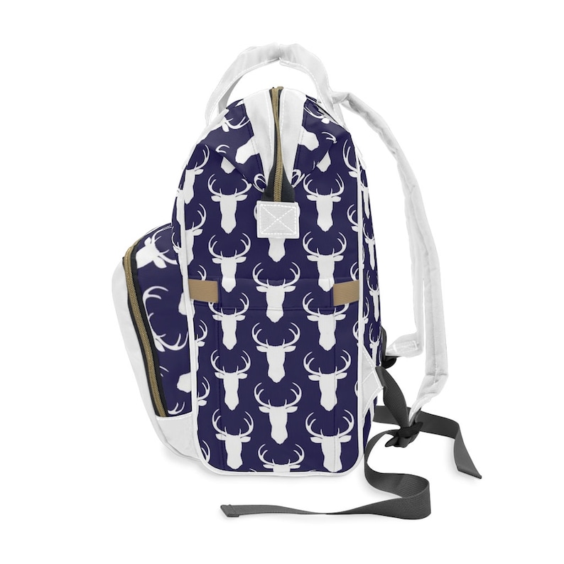 May include: A white backpack with a navy blue deer print. The backpack has a zipper closure and adjustable straps.