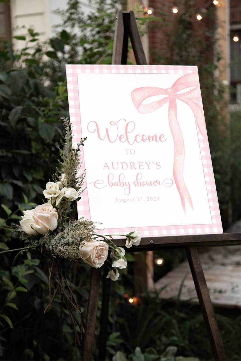 May include: A pink and white gingham welcome sign with a pink watercolor bow and the text "Welcome to Audrey's baby shower August 17, 2024".