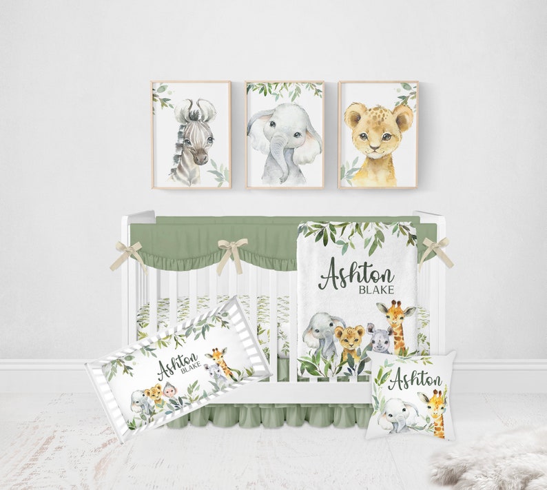 May include: A green and white crib bedding set with a jungle animal theme. The set includes a fitted sheet, a crib skirt, a blanket, and two pillowcases. The blanket features a leafy design with the names Ashton Blake. The pillowcases feature a leafy design with a giraffe, elephant, lion, and zebra.