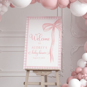May include: Pink and white balloon arch with a sign that says "Welcome to Audrey's baby shower August 17, 2024".