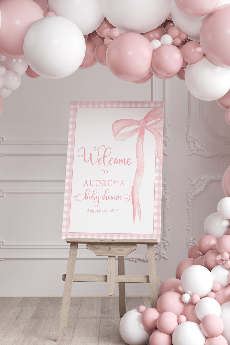 May include: Pink and white balloon arch with a sign that says "Welcome to Audrey's baby shower August 17, 2024".