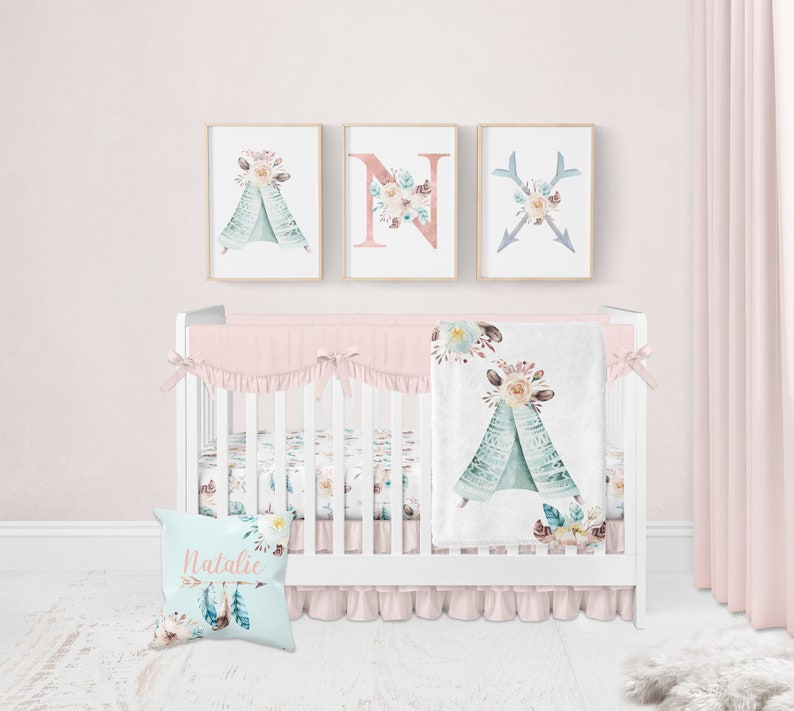 May include: A white crib with a pink and white floral crib bedding set. The bedding features a teepee design with watercolor flowers and feathers. The crib also has a personalized pillow with the name "Natalie" and a floral arrow design.