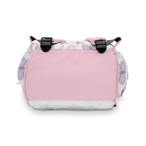 May include: A pink and white backpack with a butterfly pattern. The backpack has adjustable straps and a zip closure.