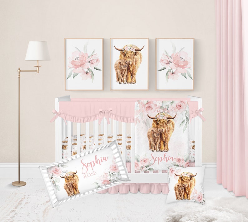 May include: A nursery set featuring a white crib with pink bedding, a floral blanket, and a decorative pillow. Above the crib are three framed prints: two with watercolor Highland cow illustrations and one with pink floral art. The set includes a personalized pillow with the name "Sophia Rose".
