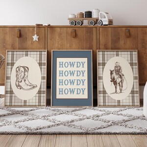 May include: Three framed prints with a Western theme. One print features a cowboy boot, another a cowboy on a horse, and the third says "HOWDY" in blue letters. The prints are on a plaid background.
