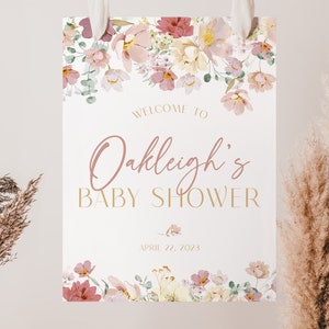 May include: A white sign with pink floral border and gold lettering. The sign says "Welcome to Oakleigh's Baby Shower - April 22, 2023".