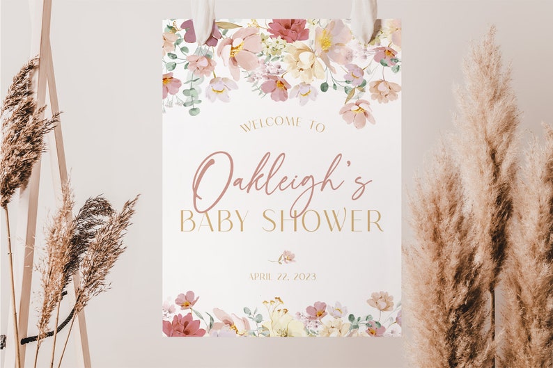 May include: A white sign with pink floral border and gold lettering. The sign says "Welcome to Oakleigh's Baby Shower - April 22, 2023".