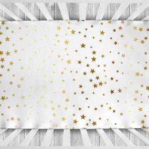 Può includere: Lenzuolo per culla bianco con un motivo a stelle dorate. Le stelle sono sparse casualmente sul lenzuolo.