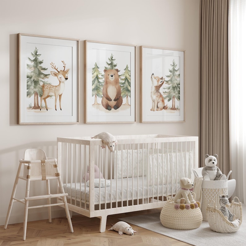 Op de afbeelding: Drie ingelijste aquarelprints van bosdieren: een hert, een beer en een vos. De prints worden weergegeven boven een witte wieg met knuffels en een kinderstoel. De kamer heeft een neutraal kleurenpalet.