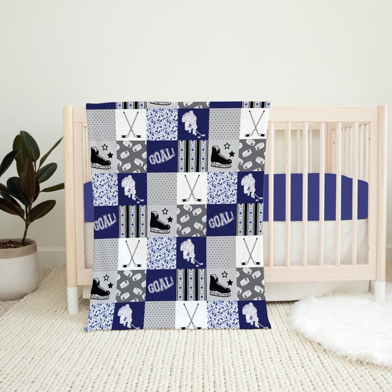 May include: A blue and white baby quilt with a hockey theme. The quilt features hockey sticks, skates, and the word "GOAL!" repeated throughout the design.
