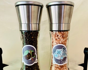 May include: Two silver metal spice grinders with black peppercorns and pink sea salt. The grinders have labels that say "Peppercorns" and "Sea Salt".