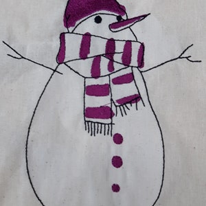 以下が含まれることがあります： 手縫いの雪だるま。紫色の帽子とマフラーをしています。雪だるまは黒いボタンが3つと黒い鼻をしています。