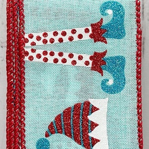May include: A blue and red ribbon with a repeating pattern of elf legs and hats. The ribbon has a red edge.