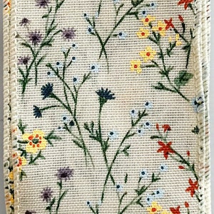 May include: A white ribbon with a floral print featuring small yellow, red, blue, and purple flowers. The ribbon has a white border.