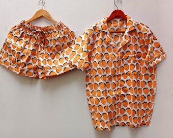 May include: A white and orange pajama set with a strawberry print. The top is a short-sleeved button-up shirt with a collar. The bottom is a pair of shorts with a drawstring.
