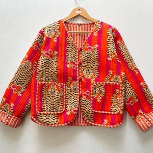 Puede incluir: Una chaqueta acolchada roja y naranja con estampado de tigre y cierre de botón. La chaqueta tiene un cuello mandarín y dos bolsillos.