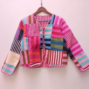 May include: A long-sleeved quilted jacket featuring a patchwork design of various striped patterns in vibrant colors including pink, blue, yellow, and brown. The jacket has a V-neckline, a front button closure with three small buttons, and a straight hem.