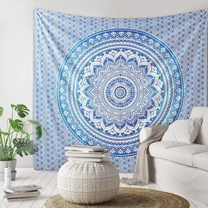 May include: A blue and white mandala tapestry with a large, intricate mandala design in the center. The tapestry is hanging on a white wall and there is a white couch and a white ottoman in the foreground.